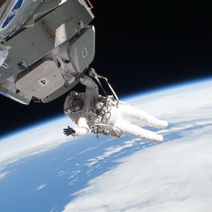 An astronaut floating in space, holding onto a piece of a man-made sattelite