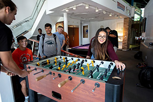 Laughing girl playing foozeball while other students watch