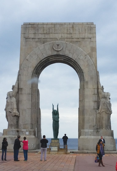 A statue with uplifted arms under a massive stone arch