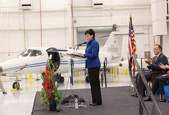 A person speaks from a podium at the front of the airplane hangar