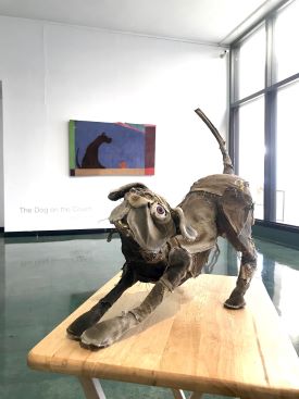 A sculpture of a dog made of stell, leather and plastic. The dog is doing a downward dog pose.