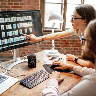 woman pointing to computer screen with photos. Man looking on.